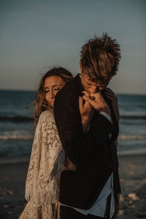 groom-kissing-bride-hands-beach-blue-ocean-boho-beach-elopement-photographer-outerbanks-north-Carolina.jpg