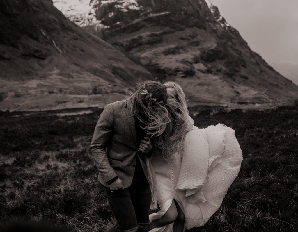 Black and white photo of bride and groom windswept and walking.