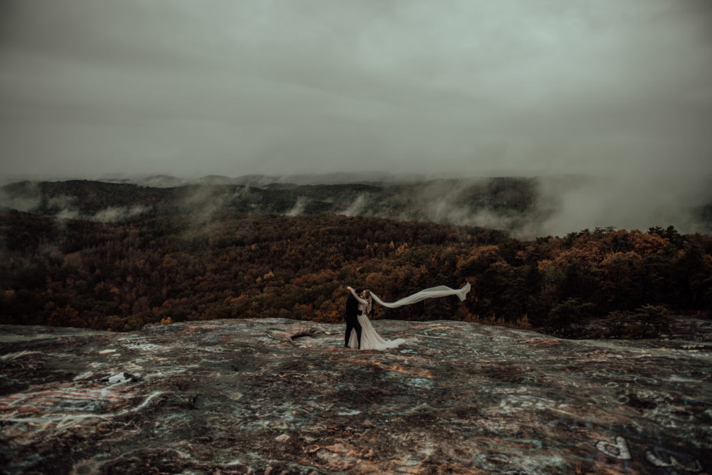 Bride and groom hugging and bride's veil flowing taken on a mountain top elopement in north carolina 