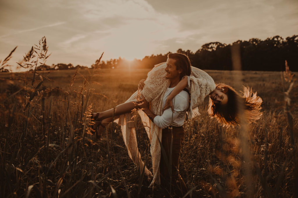 Photo of the guy picking the girl up on his shoulder and spinning her with sunset light shining in her hair 