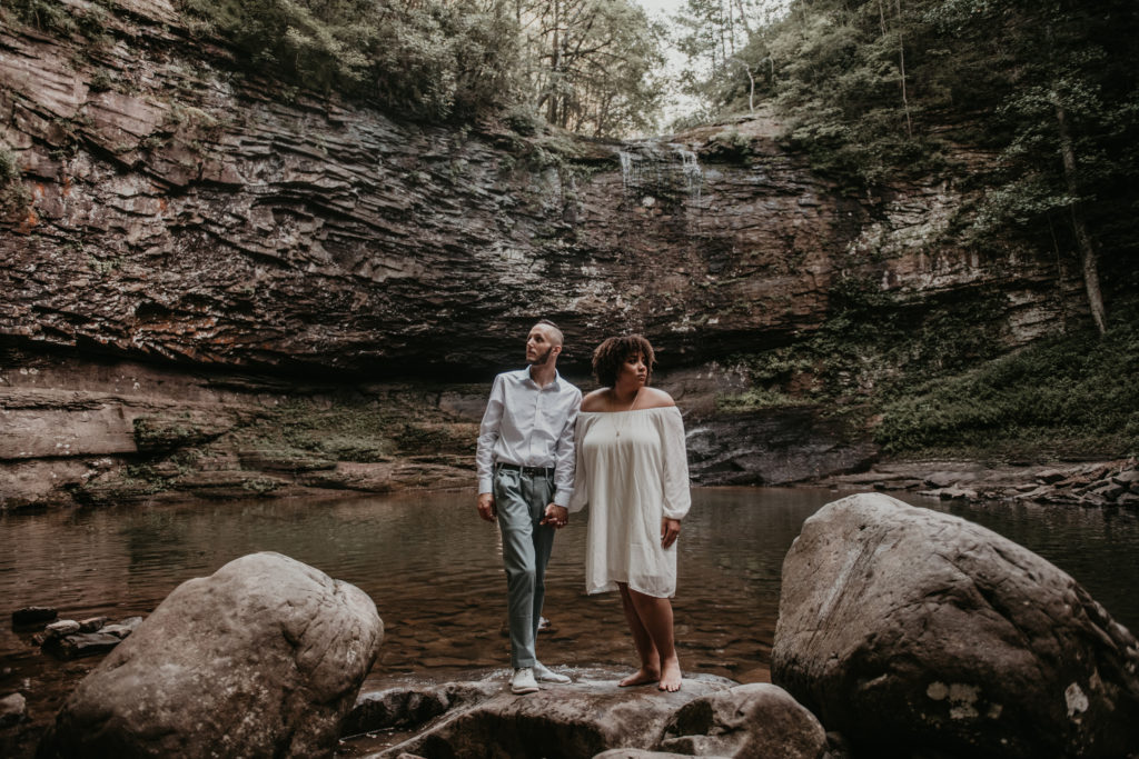 bride and groom standing on a rock, holding hands and looking in the opposite direction in front of a waterfall at Cloudland canyon in Georgia
