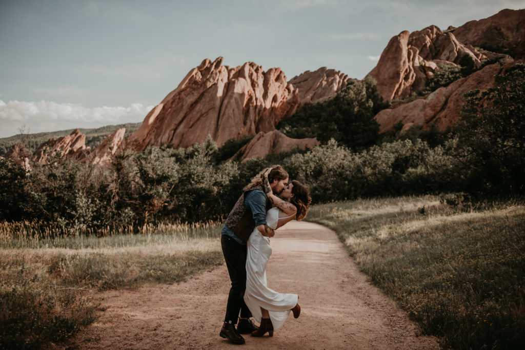 bride and groom holding each other, hugging and kissing in front og the red rocks in colorado