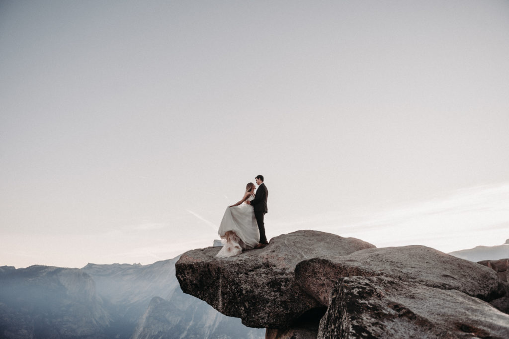 Bride and groom standing at the ends of a cliff and looking at each other taken at Yosemite