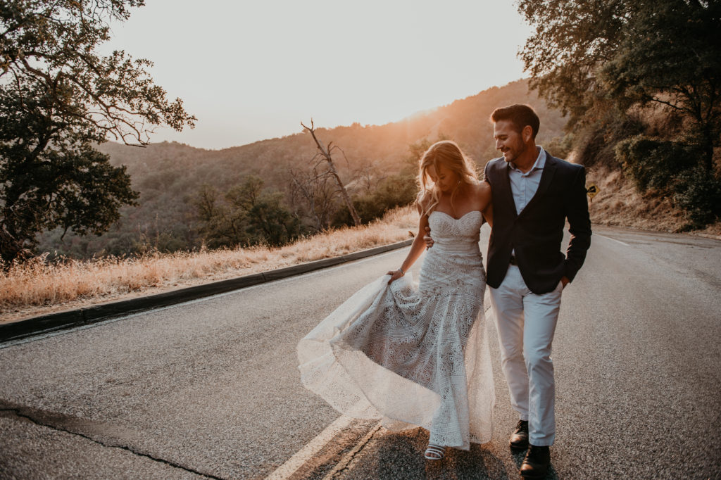 bride and groom holding each other and walking on a mountain roadand bride swinging her dress during sunset
