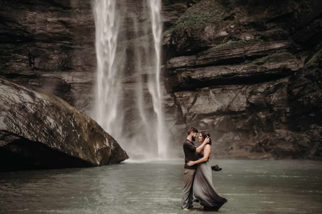 groom brushing the brides hair from her face in front of a waterfall at Toccoa falls in georgia