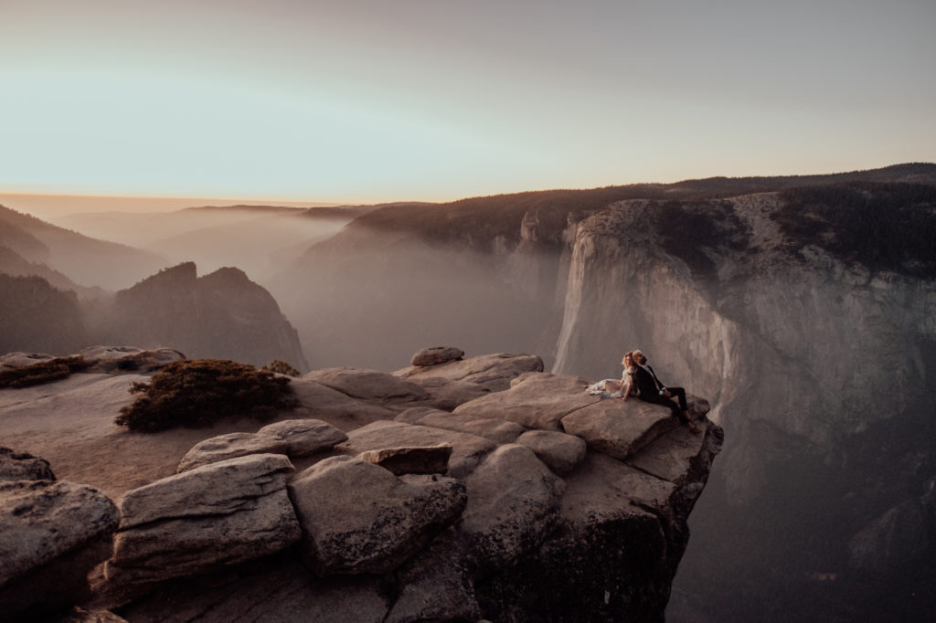 bride and groom sitting back to back at the edge of the cliff at Yosemite national park