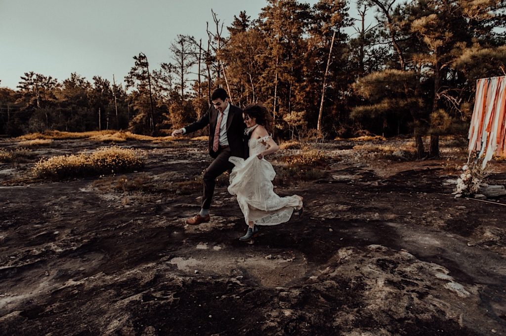 bride and groom holding hands and running and jumping over puddles taken at an arabia mountain elopement
