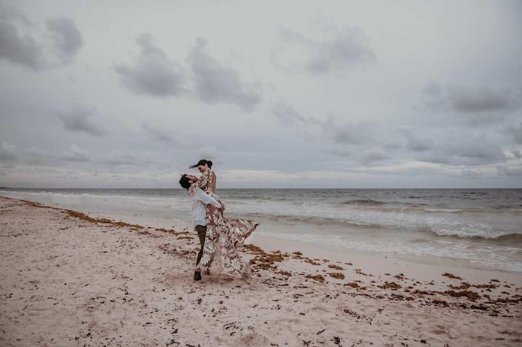 Photo of the groom picking up the bride and twirling her on the beach taken at an elopement in Tulum Mexico