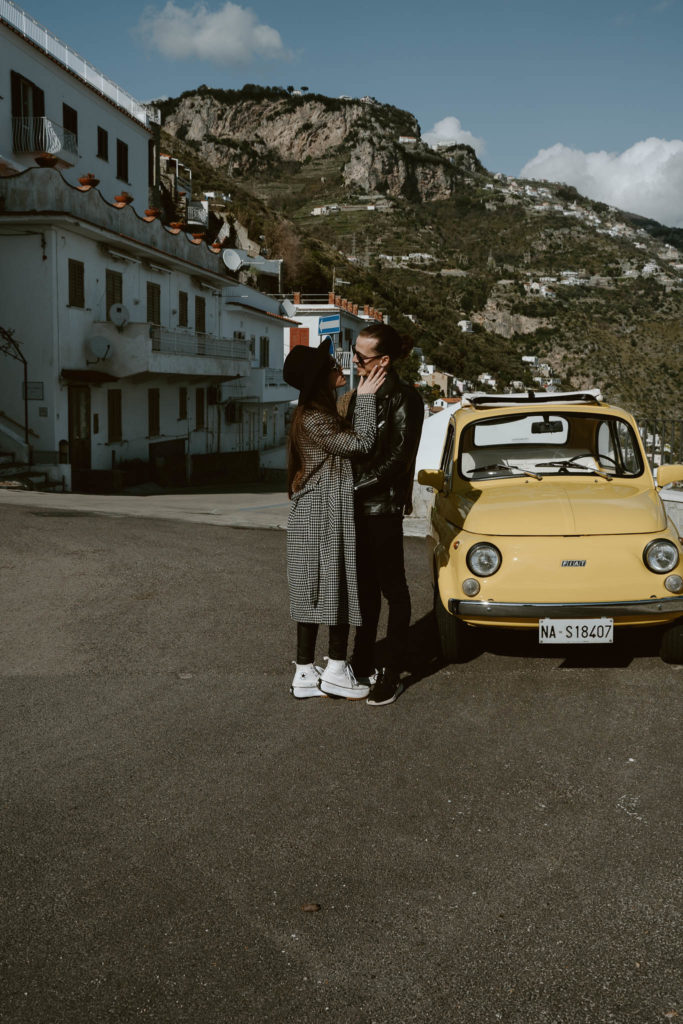 Couple standing next to a yellow vintage fiat and looking at each other taken on the streets of Amalfi