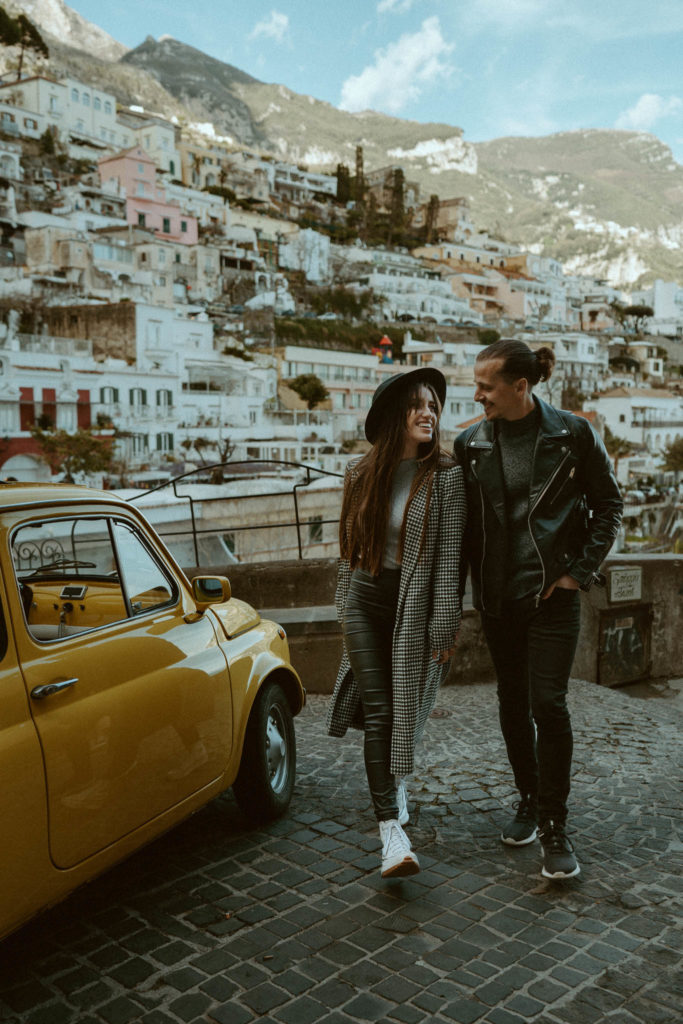 Couple walking and laughing towards the frame next to a yellow vintage car