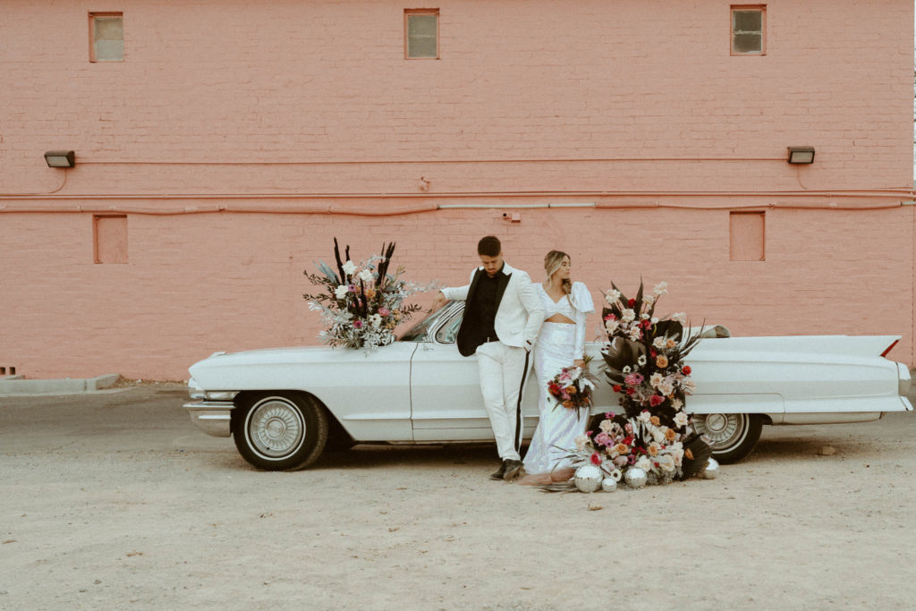 bride and groom standing in front of a pink wall with the vintage car on freemont street in Las Vegas