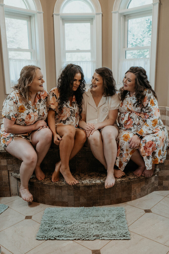 Bride and bridesmaids in pajamas sitting on bathtub