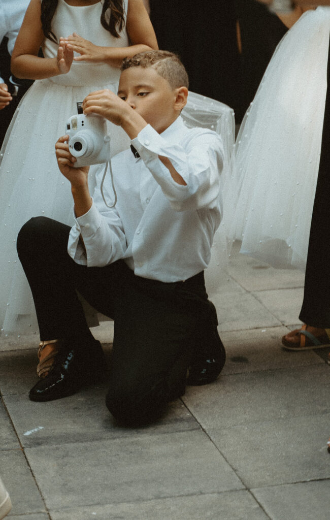 Little boy taking a polaroid picture of bride and groom dancing