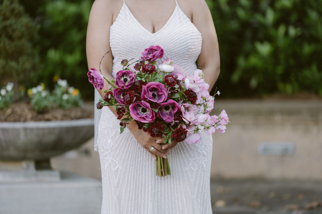 Close up photo of a bride holding a purple wedding bouquet. 