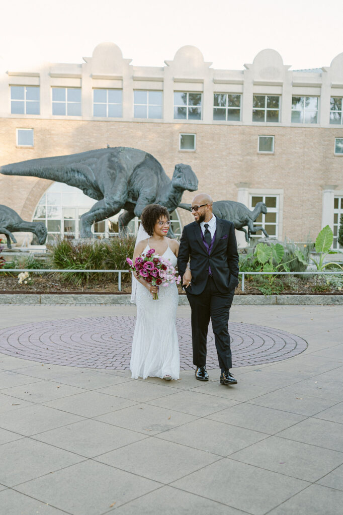 Bride and groom posing in front of dinosaur sculptures for their Fernbank Museum wedding photos in Atlanta, Georgia. 