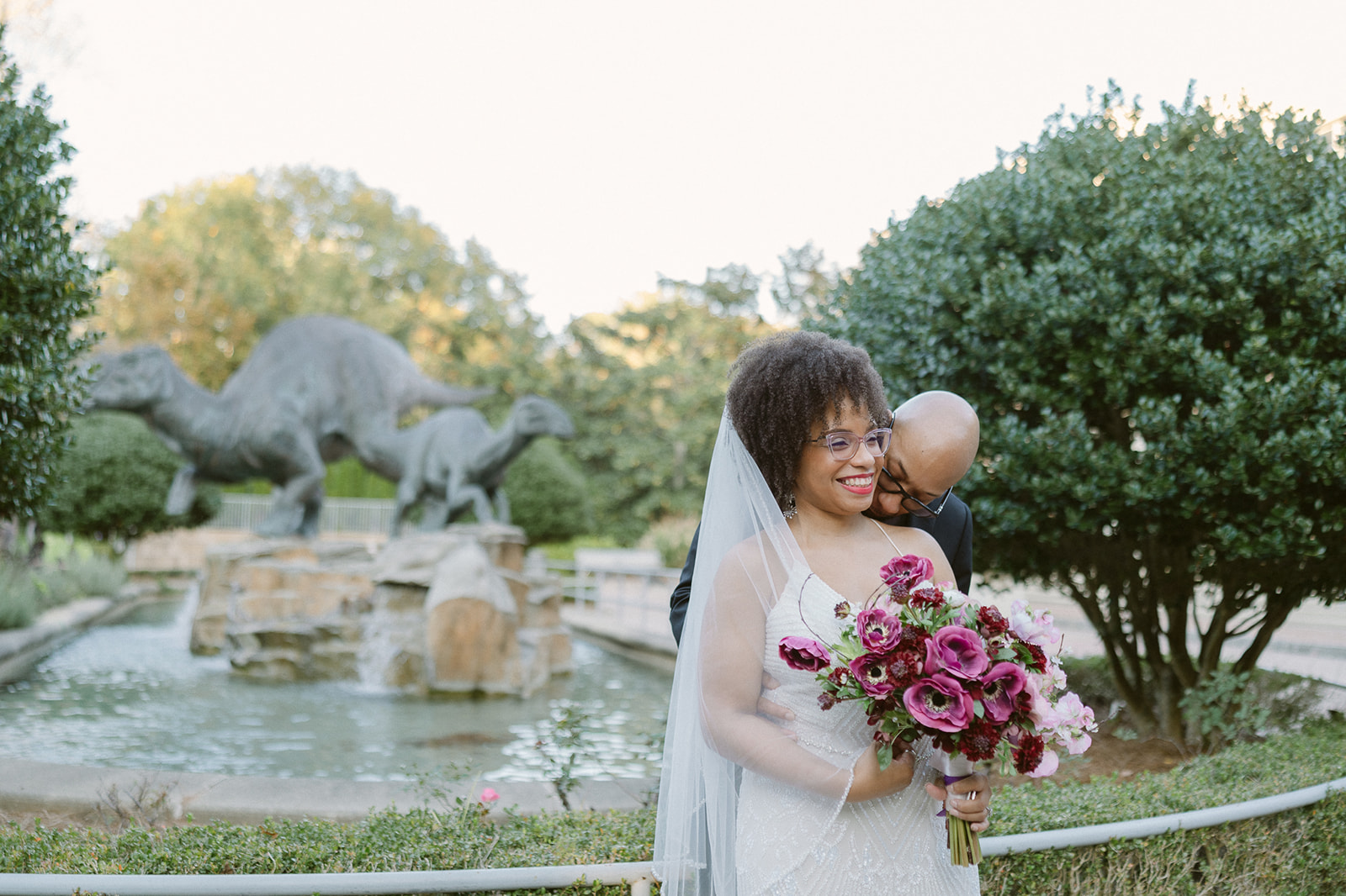 Bride and groom posing in front of dinosaur sculptures for their Fernbank Museum wedding photos in Atlanta, Georgia. 