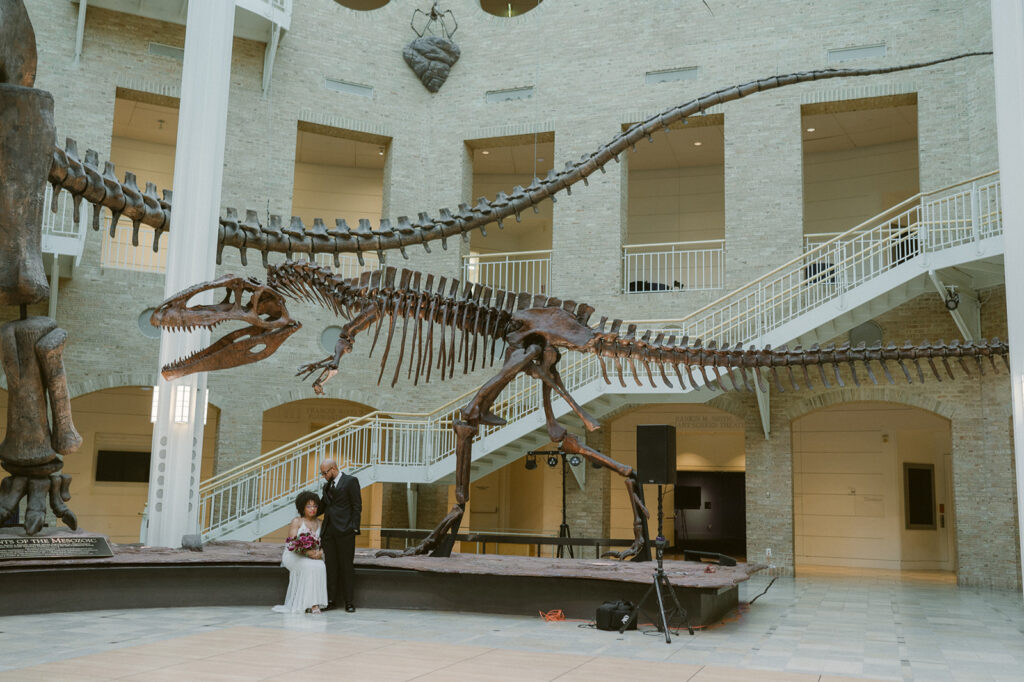 Bride and groom posing for photos with dinosaur in the Great Hall of Fernbank Museum wedding venue in Atlanta, Georgia