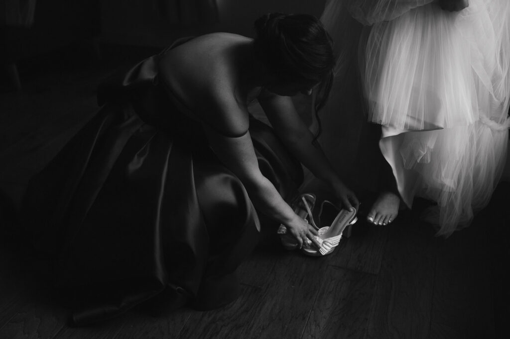 Black and white photo of a bridesmaid putting brides shoes on