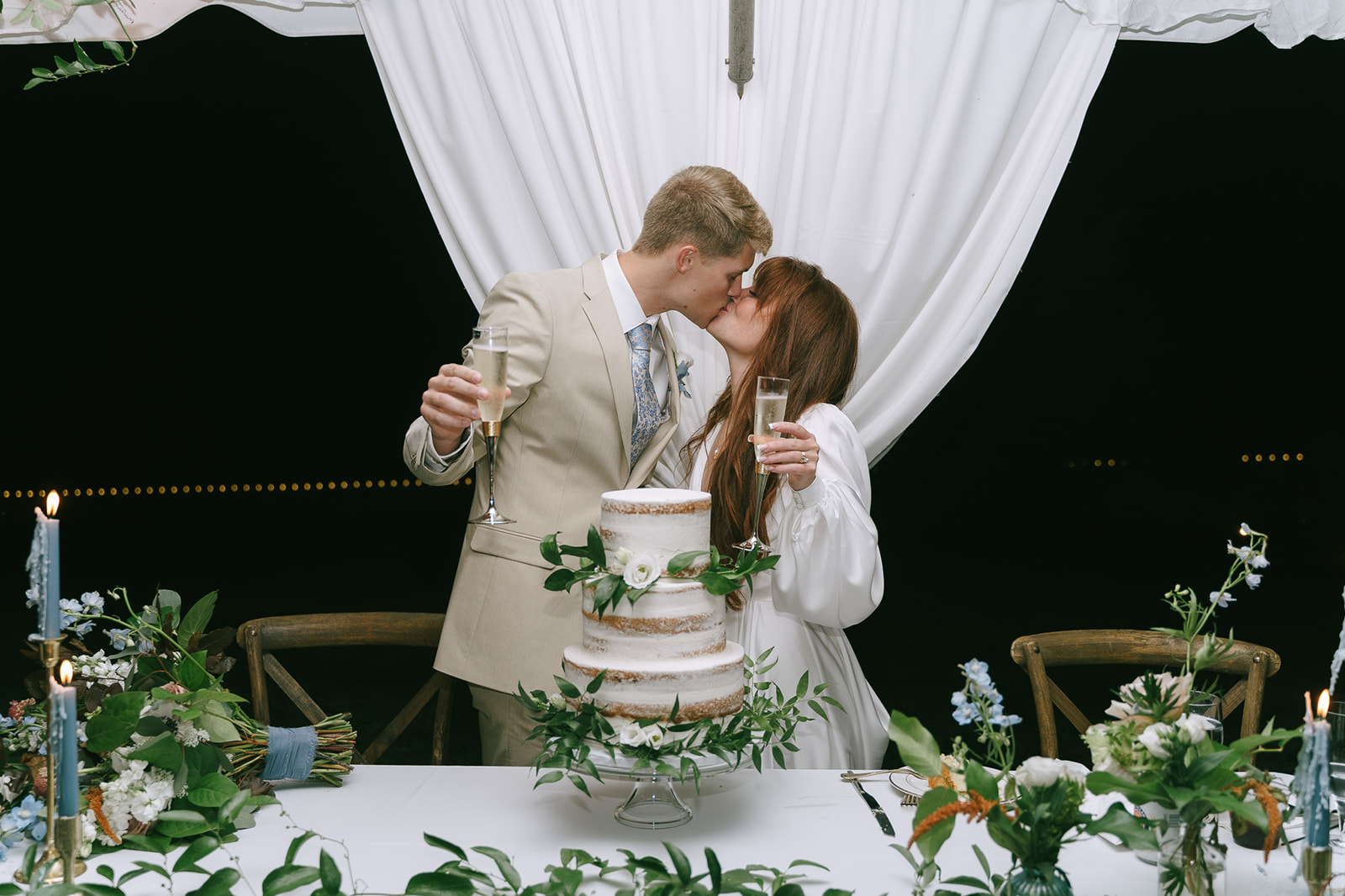 Bride and groom kissing as they hold up their champagne glasses at the end of the night. - Planning The Perfect Wedding Photography Timeline