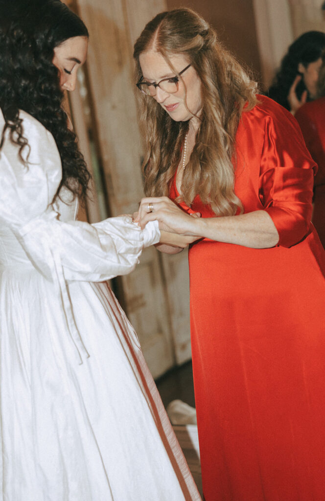 mother of the bride helping her with the jewelry before the coquette themed wedding ceremony